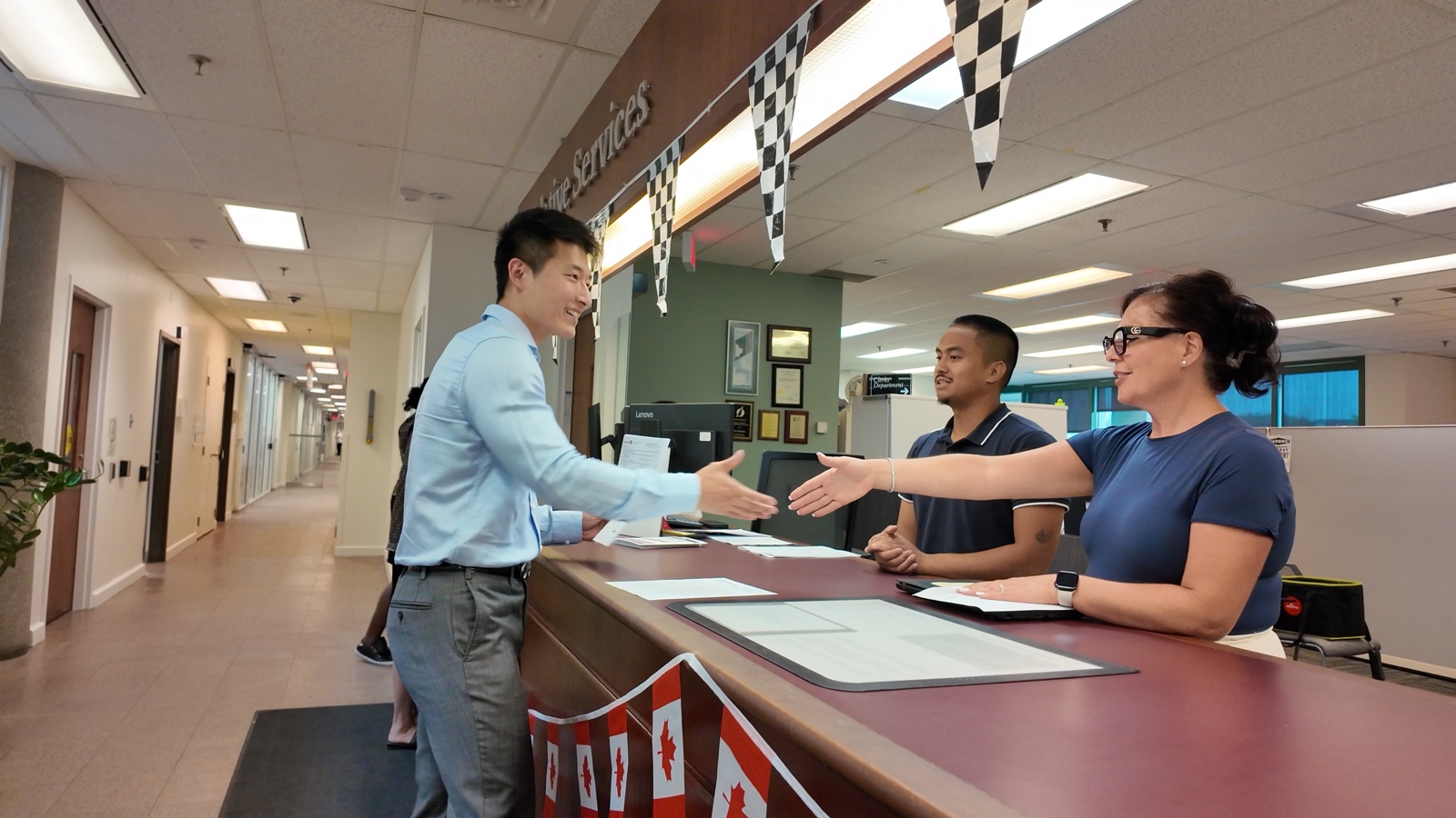 Haohui Yu shaking hands with a clerk across the Legislative Services counter after filing his nomination papers